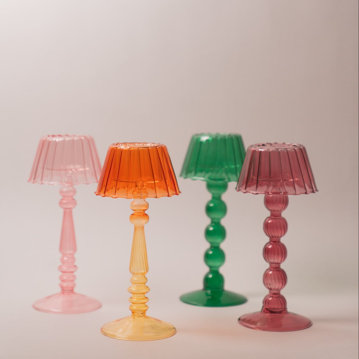 Four colourful lamp-style glass tealight holder on a plain background