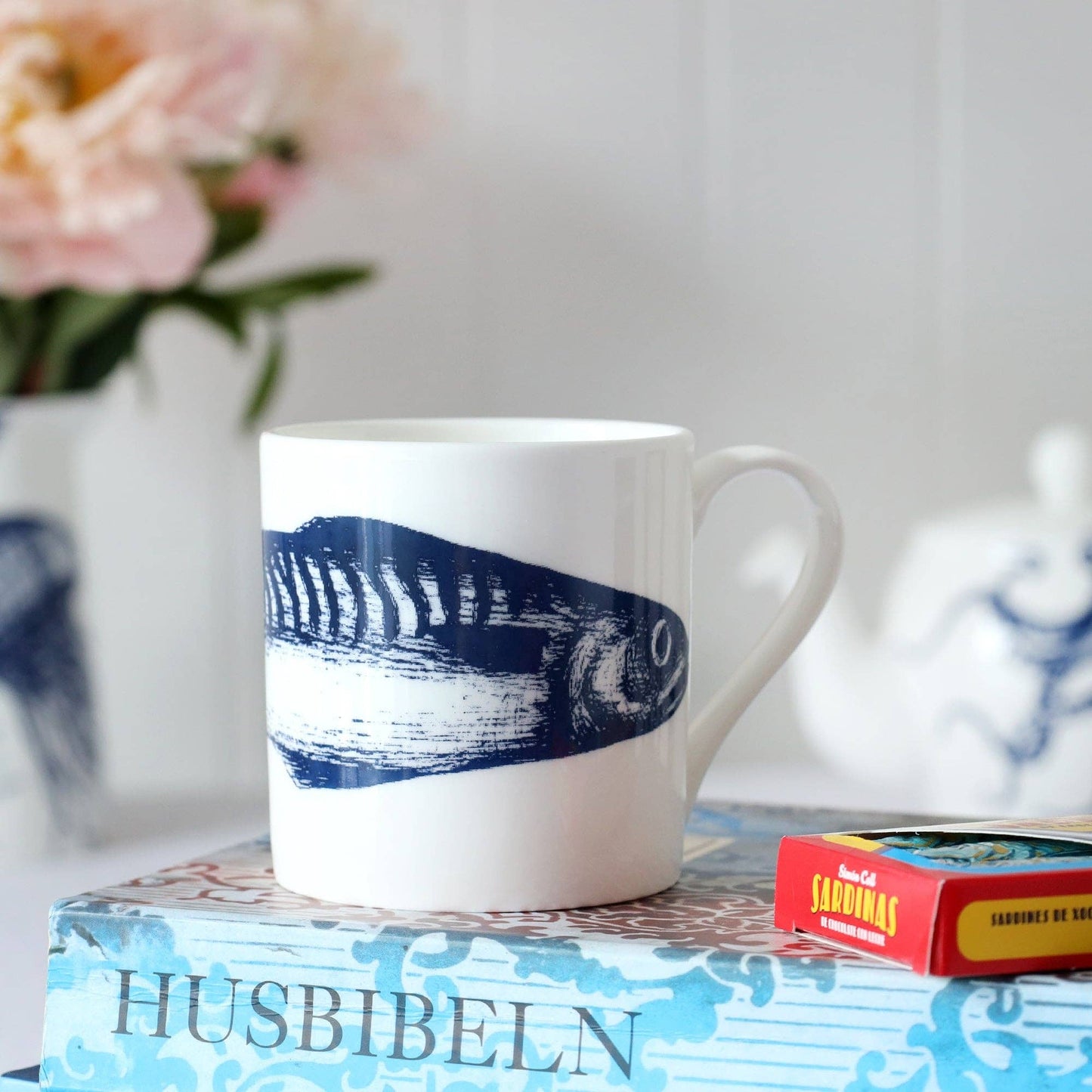 Close up of mug on top of a book "Husbibeln" text is on spine of book - illustration of fish head in shot.