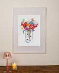 Framed artwork of colourful flowers on a wall with a lamp and candle below. Edinburgh artist Kirsty penny