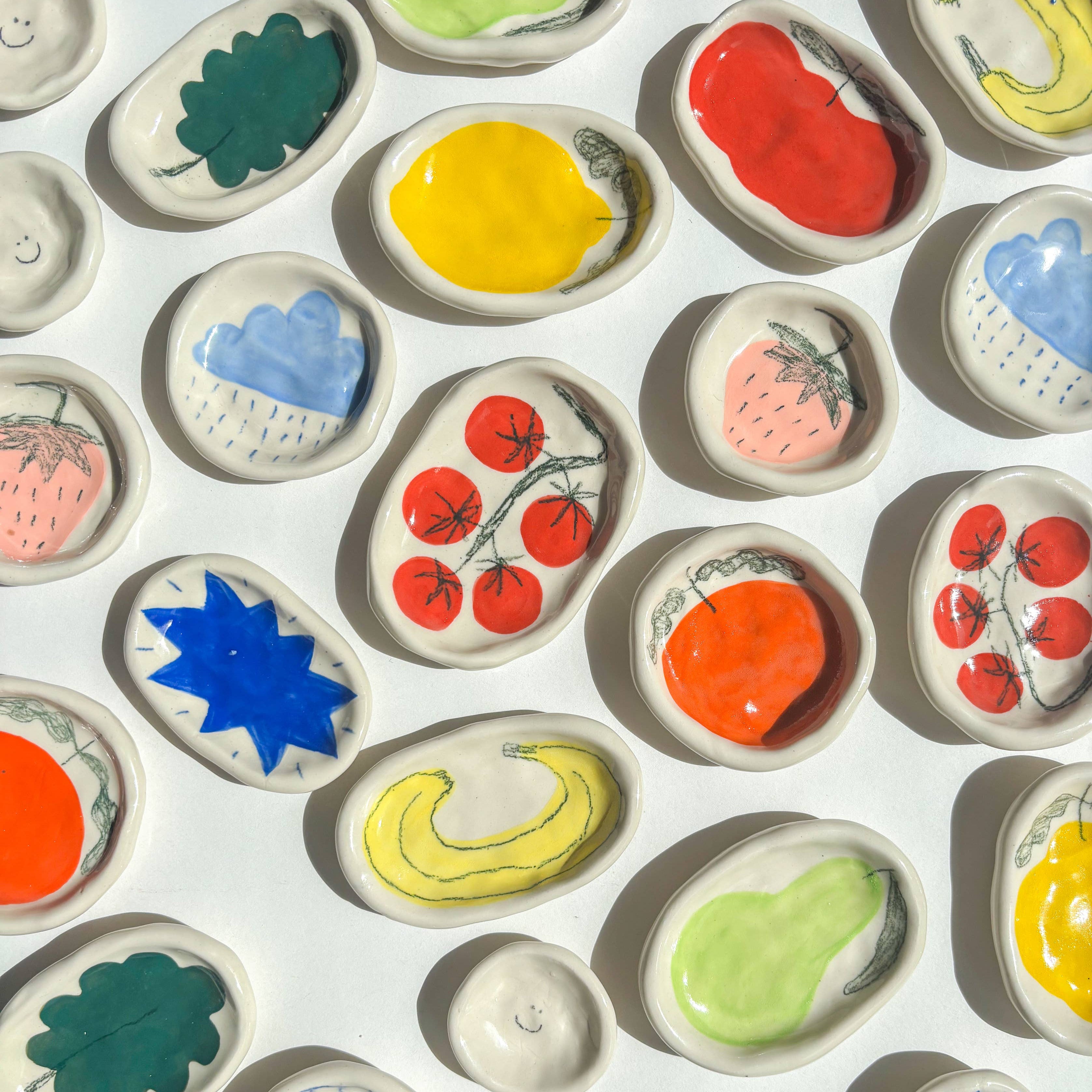 Assortment of colourful ceramic dishes with various designs on a white background. Handmade gifts.