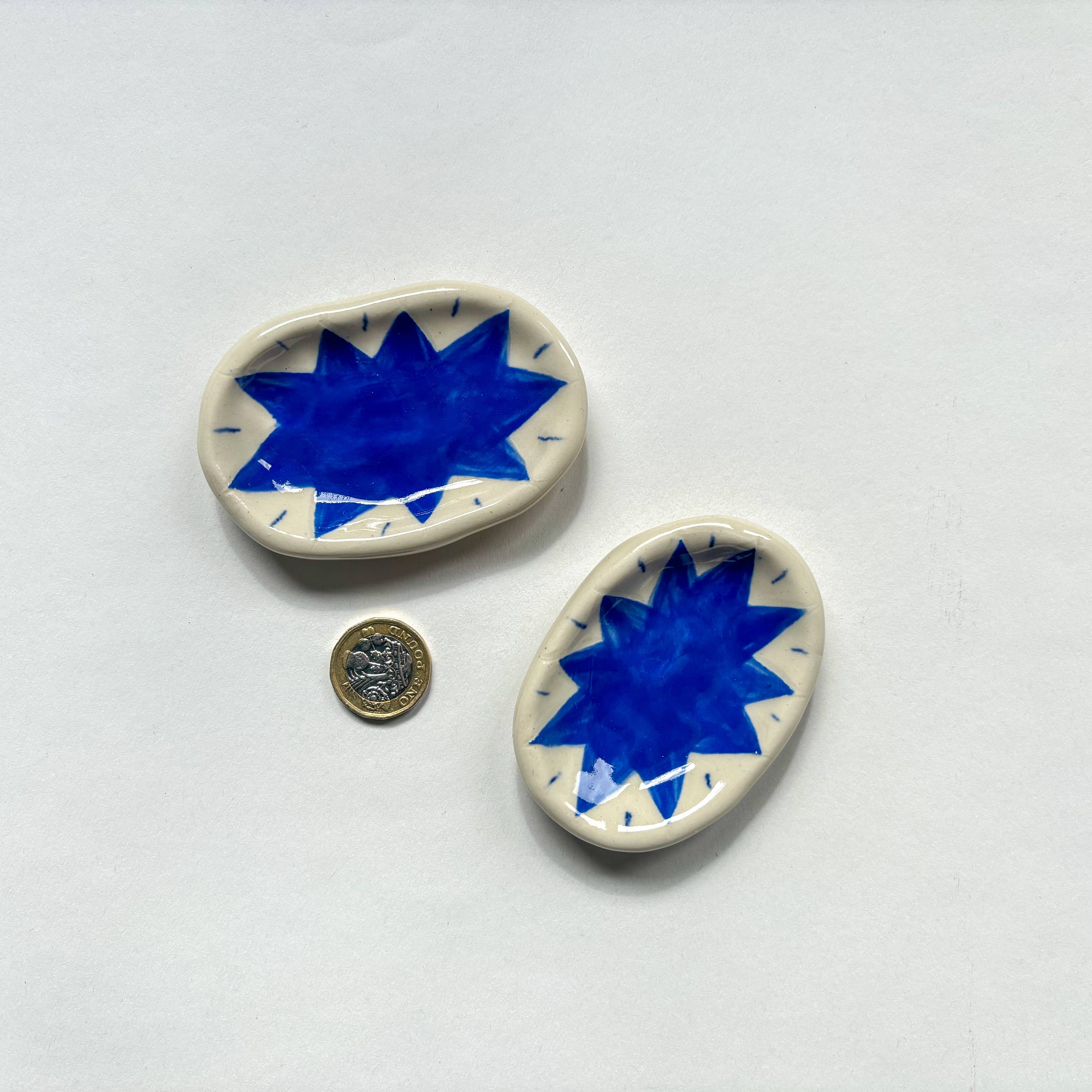 Two  handmade ceramic dishes with blue splat design  are shown beside a pound coin for scale. Handmade unique gifts.