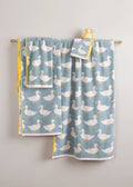 Set of pale blue towels with duck pattern hanging on a rail against a light backround. Small rubber yellow duck is balanced on the top.