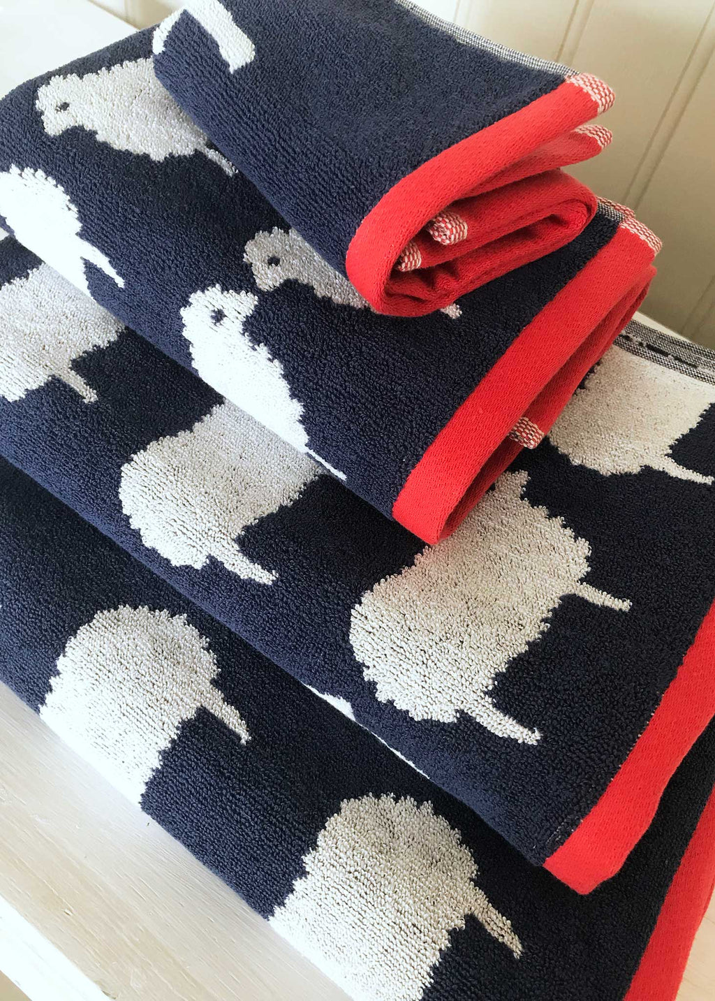 Folded navy Kissing Sheep towel  with white sheep design and a red trim. 