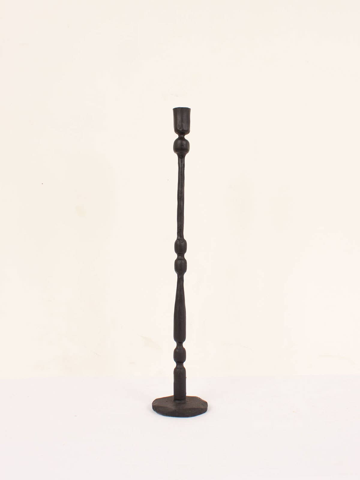 Single tall tall iron candlestick on white studio background. Eliot candlestick handcrafted in India using traditional techniques.