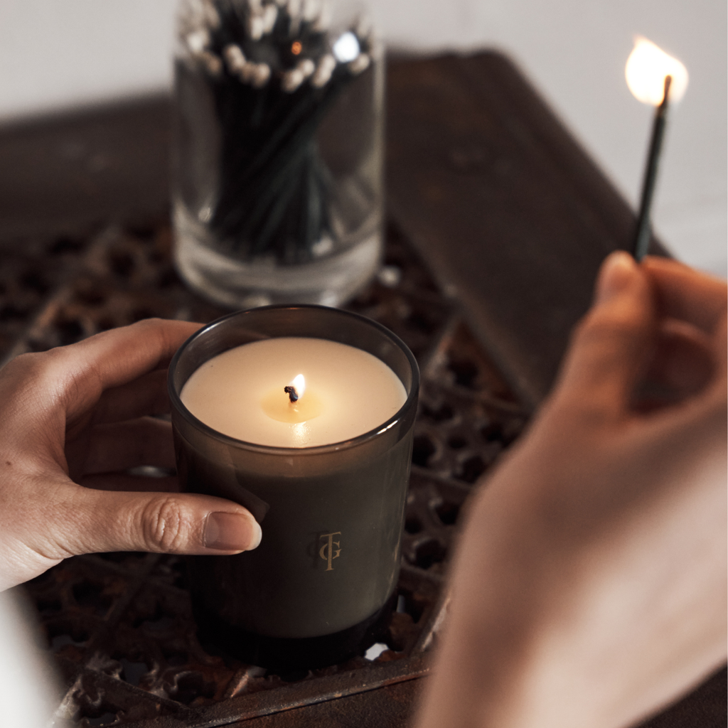 Candle being lit. Models two hands in shot striking a match and a jar of luxury white tipped matches are visible.