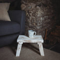 Interior shot by stone fireplace and navy armchair of white stool with a mug on the top.
Folding whitewashed stool - perfect for resting a mug on.Made in India and ethically sourced.