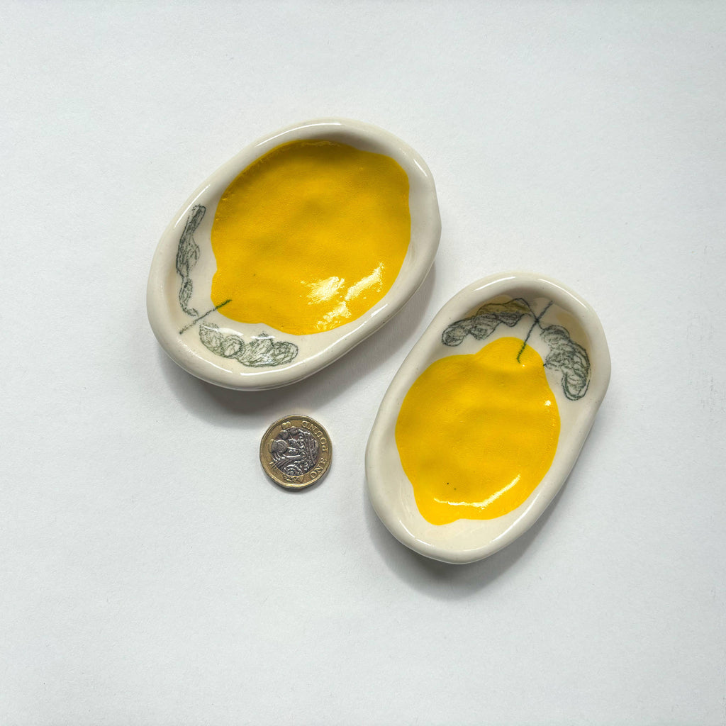 Two  handmade ceramic dishes with yellow lemon design  are shown beside a pound coin for scale. Handmade unique gifts.