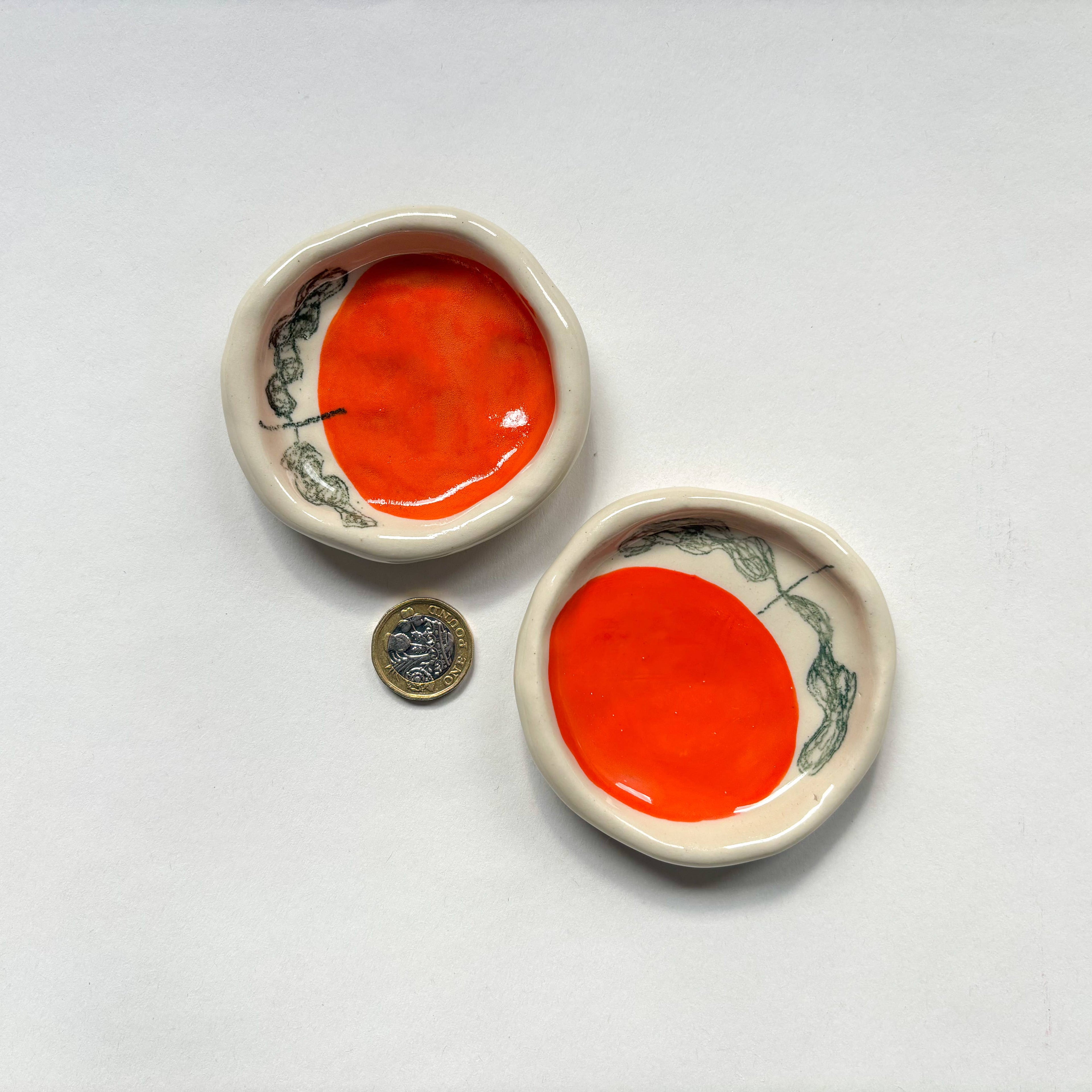 Two  handmade ceramic dishes with an orange design  are shown beside a pound coin for scale. Handmade unique gifts.