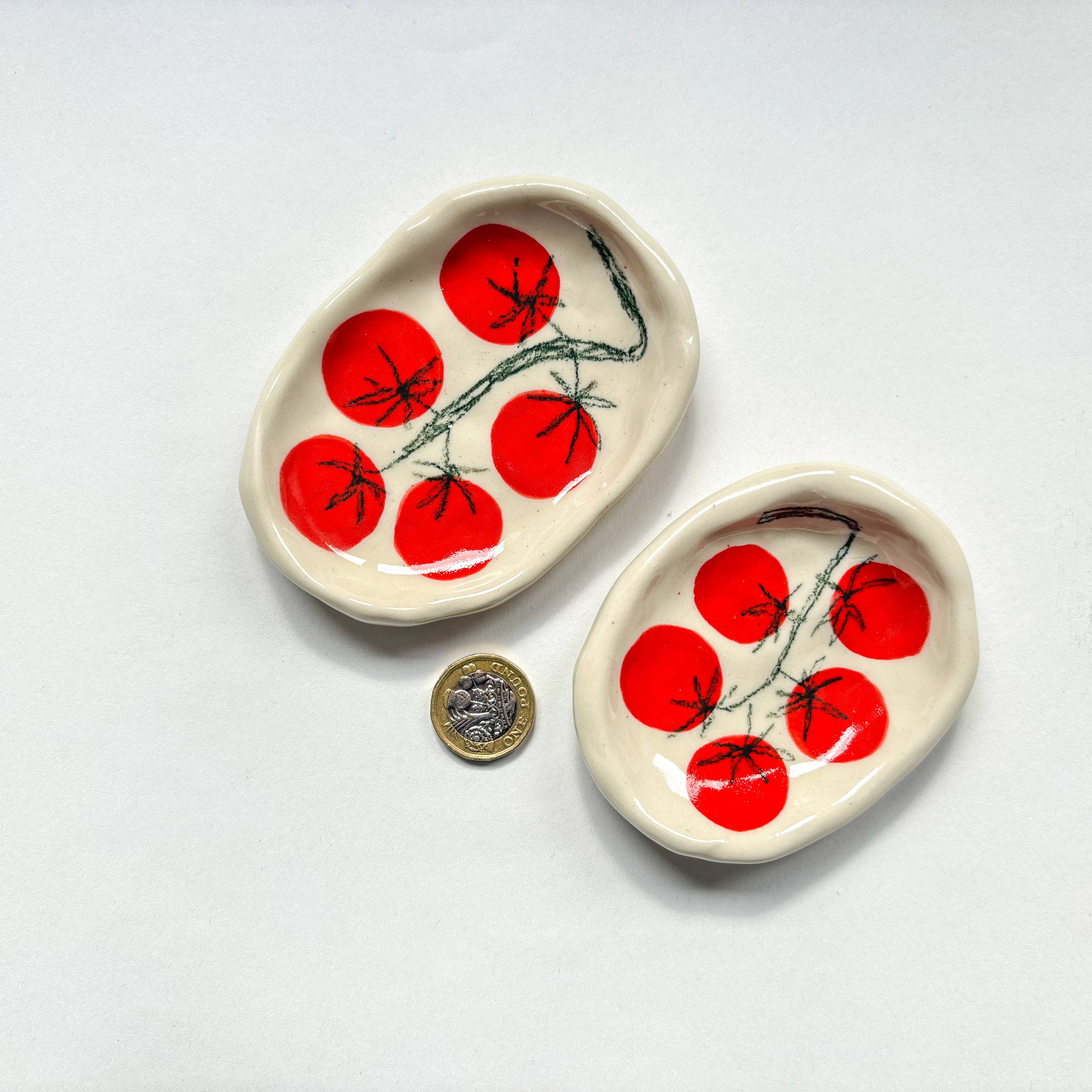 Two  handmade ceramic dishes with red tomatoe design  are shown beside a pound coin for scale. Handmade unique gifts.