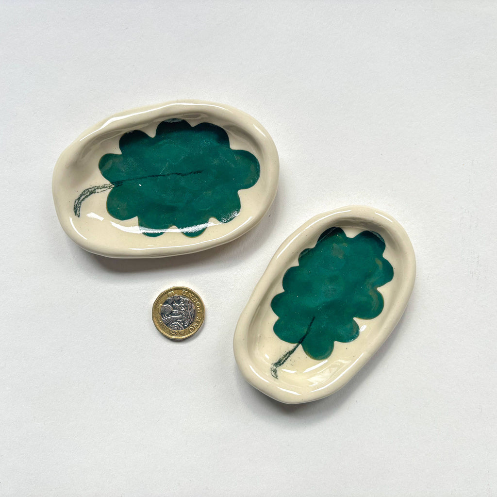 Two  handmade ceramic dishes with a green leaf design  are shown beside a pound coin for scale. Handmade unique gifts.