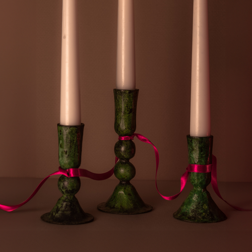 Close up of three green verdigris candlesticks showing the patina and design of each one. They are linked together by a hot pink silk ribbon .
Ethically produced iron candlesticks.