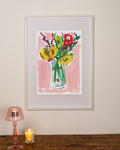 Framed artwork of a floral still life on a wall with a lamp and candle below.