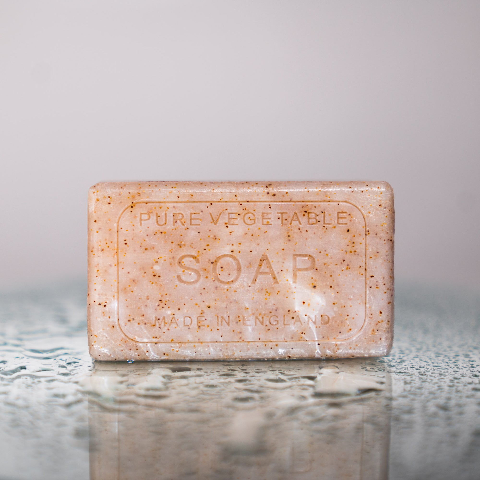 unwrapped bar of soap on water droplet reflective surface. Soap reads 'PURE VEGETABLE SOAP MADE IN ENGLAND'