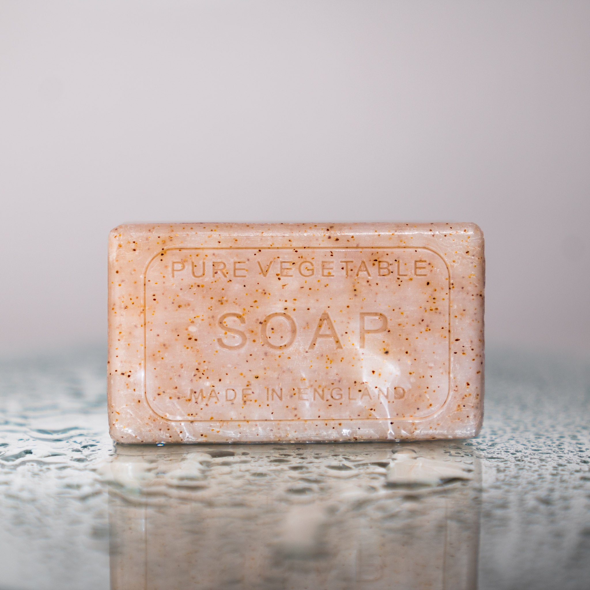 unwrapped bar of soap on water droplet reflective surface. Soap reads 'PURE VEGETABLE SOAP MADE IN ENGLAND'