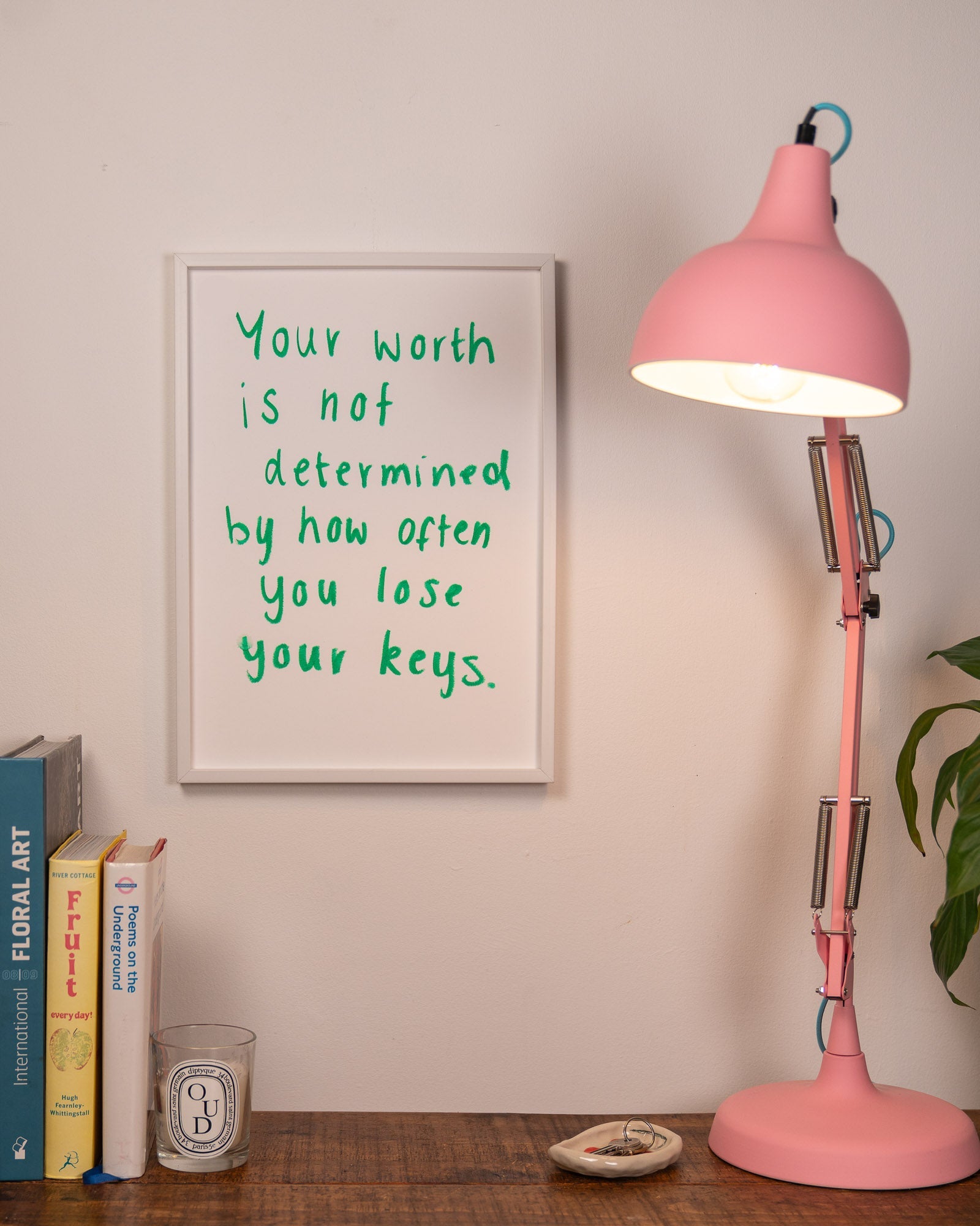Pink lamp with blue chord on a wooden surface with a motivational quote poster in the background.