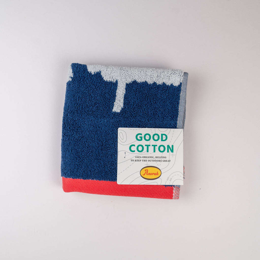 Folded blue and red towel with a Good Cotton label on a light gray background. Kissing sheep face cloth made by Anorak