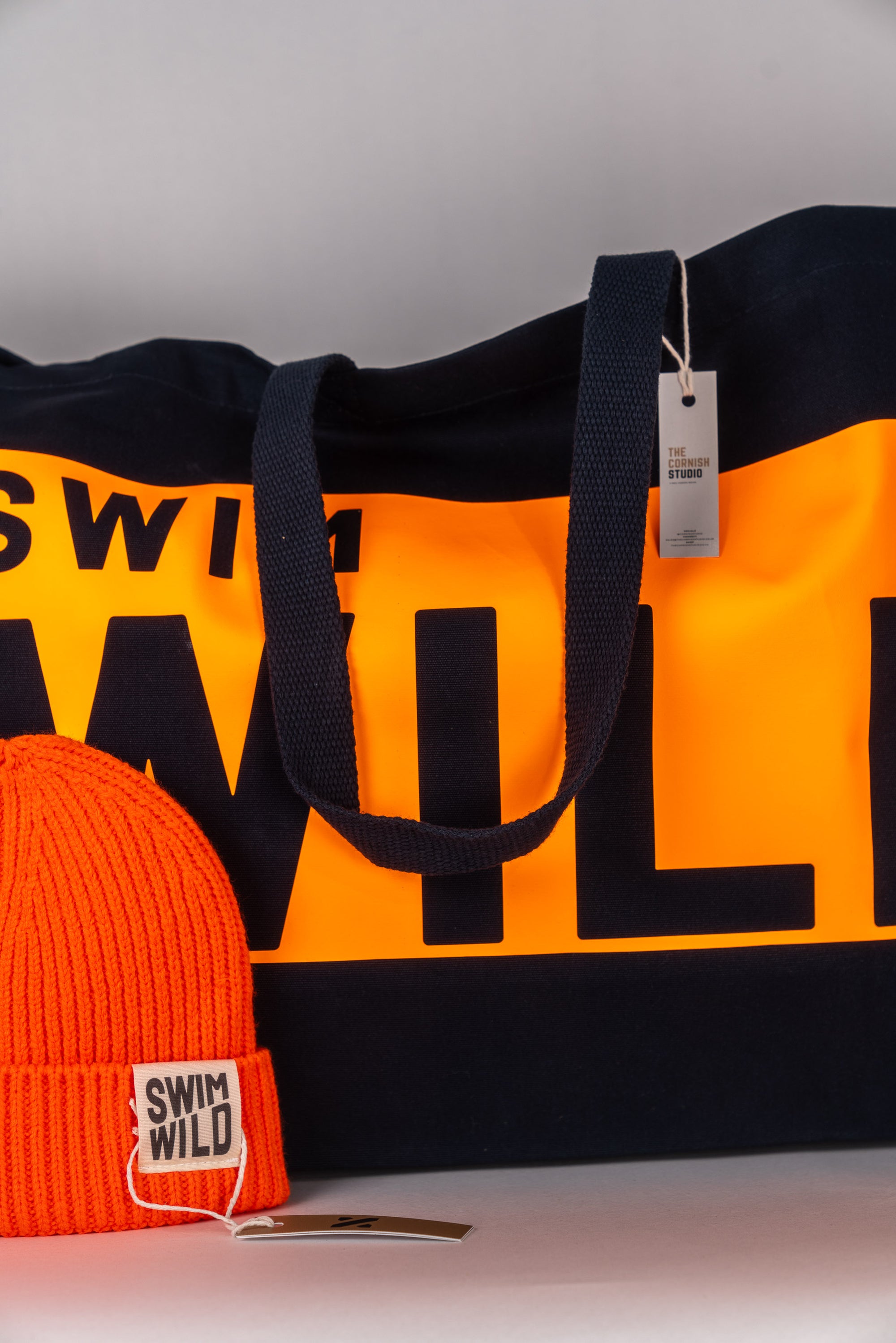Close up of Wild Swim jumbo bag in navy and orange and orange Wild Swim hat.