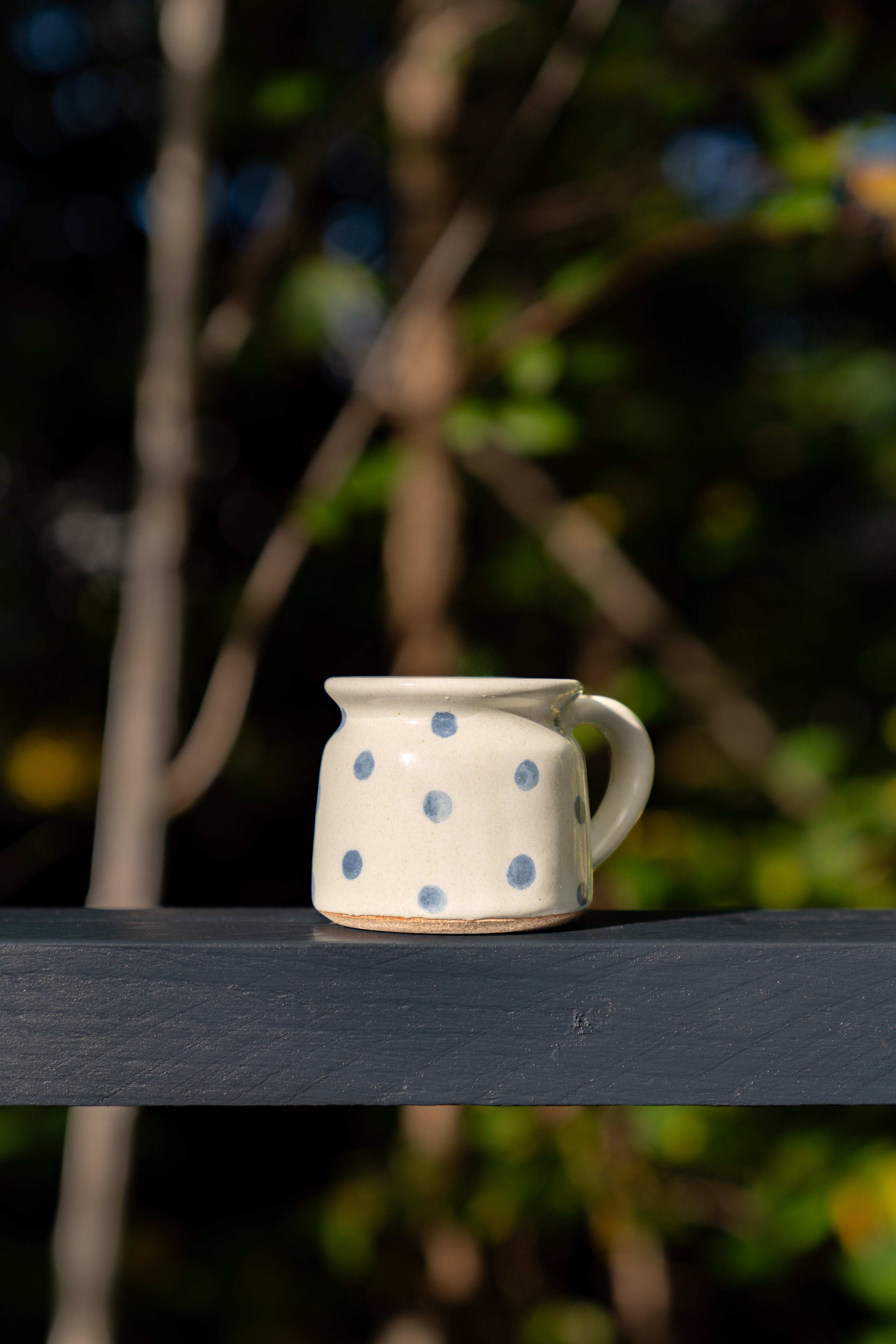 Outdoor shot of Fairtrade blue polka dot mug in sunlight with trees in background. Fairtrade gifting.