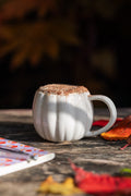 Pumpkin shaped mug on outdoor table with autumn leaves.Filled with cinnamon topped drink.