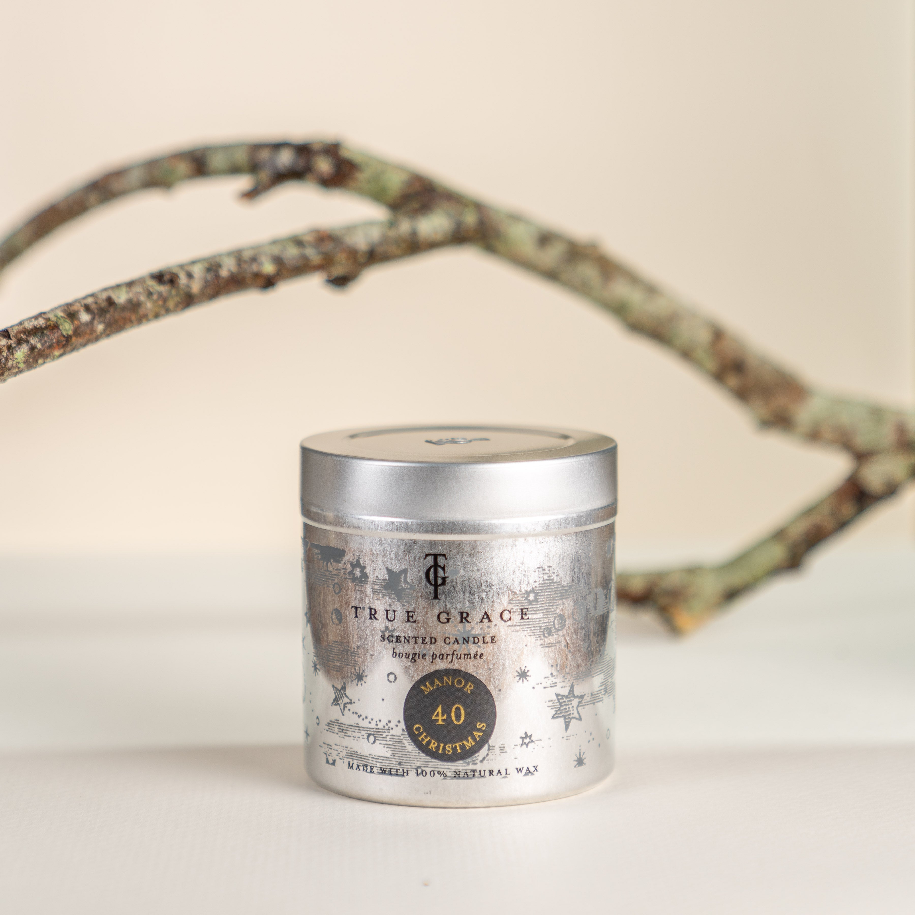 True Grace Manor Christmas Candle in a Tin Number 40. Cream background and branch in background.