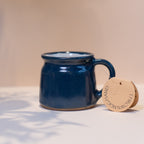 Hand made navy blue ceramic mug on a light warm coloured backround. Mug label reads  'THROWN.MUG.HAND' 