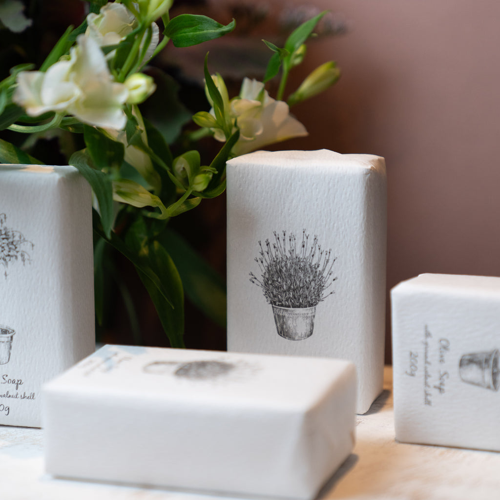 Four soaps wrapped in white with botanical illustrations and a white flower.