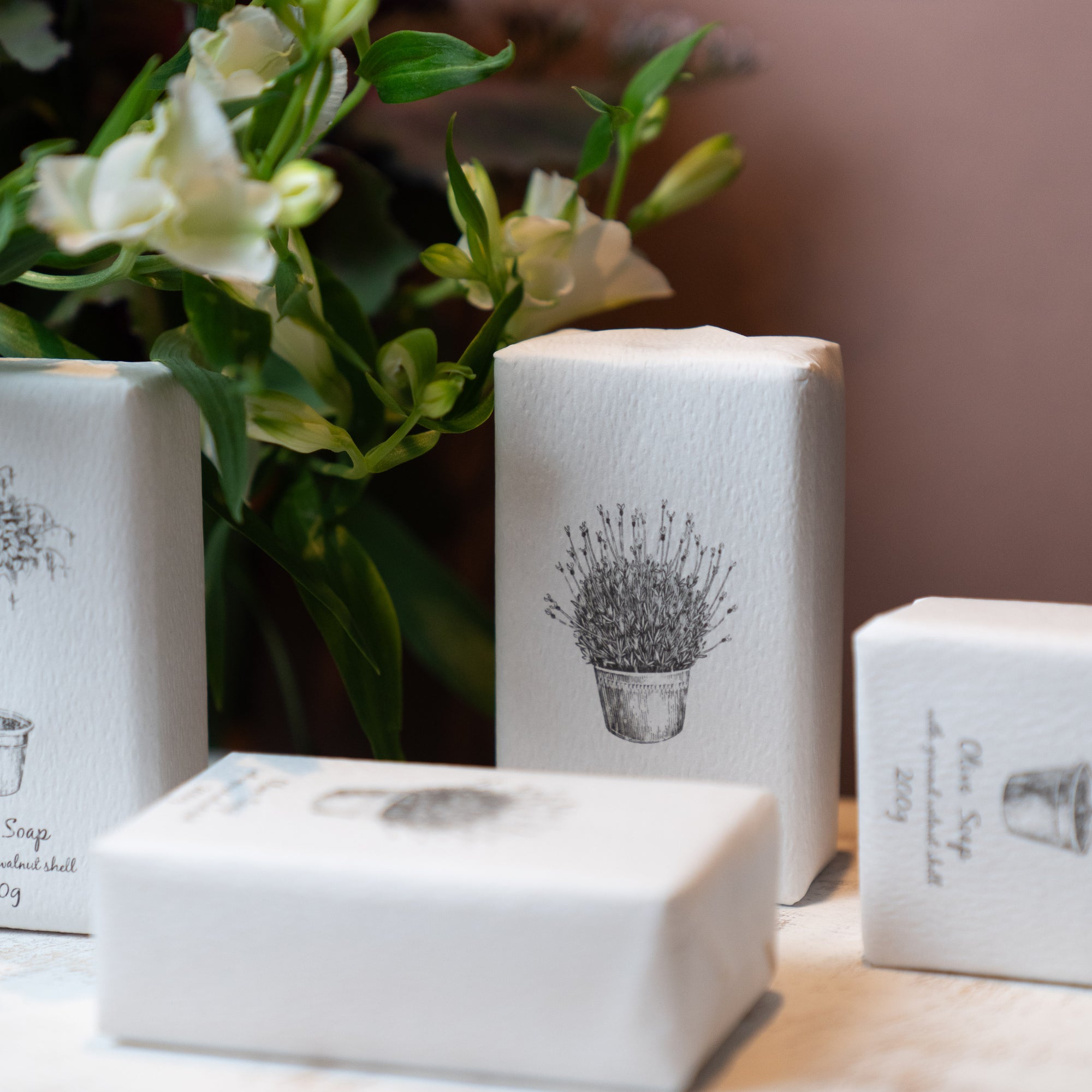 Four soaps wrapped in white with botanical illustrations and a white flower.