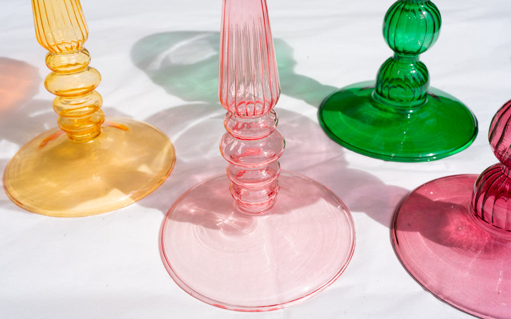 Colorful glass candle holders on a white surface, close up of the bases with shadows on white background