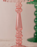 Close-up of a pink lamp-style glass tealight holder with a ribbed design on a light background.