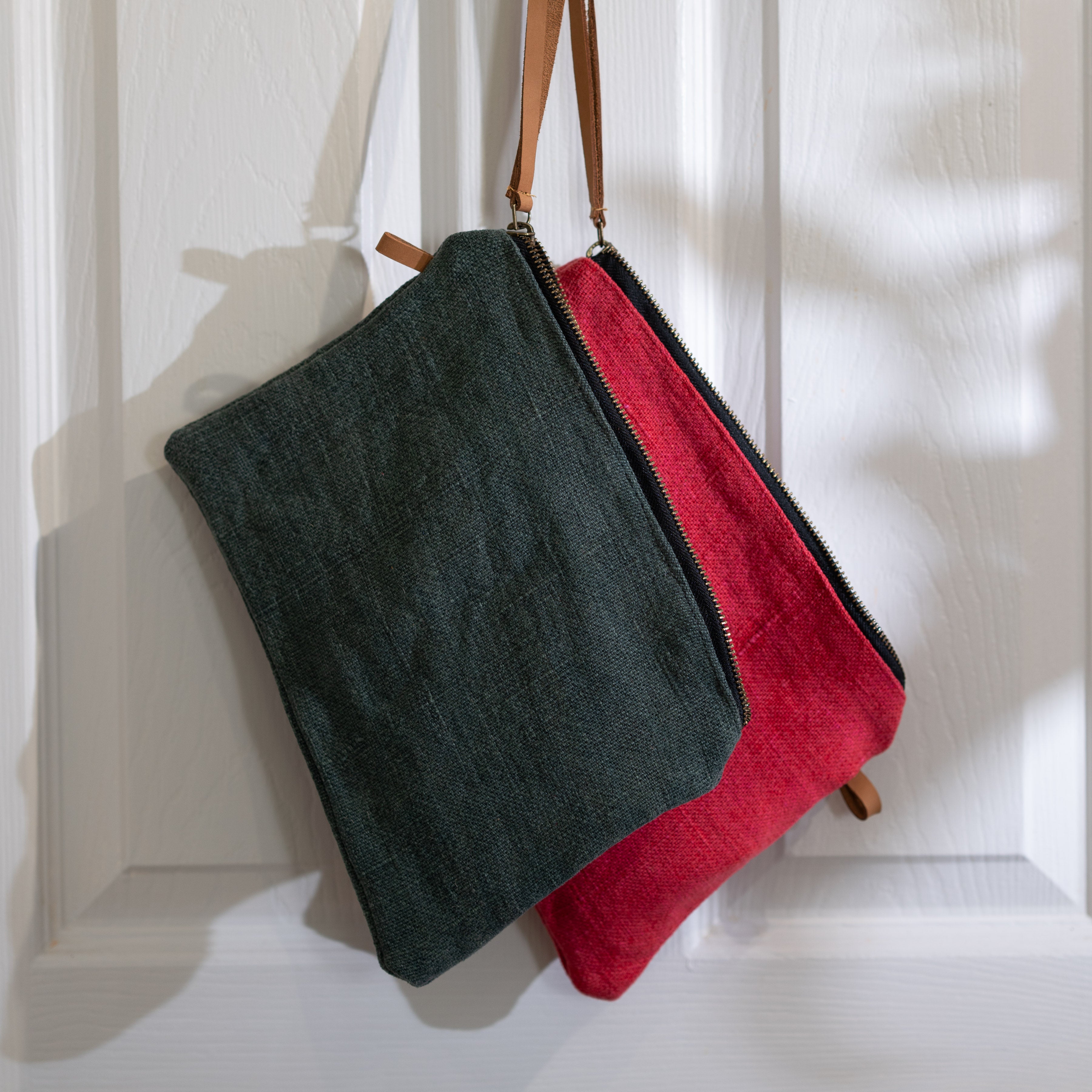 Grey and red jute bags with leather strap hanging on white door.