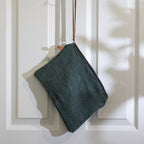 Grey jute bag with leather strap hanging on white door.