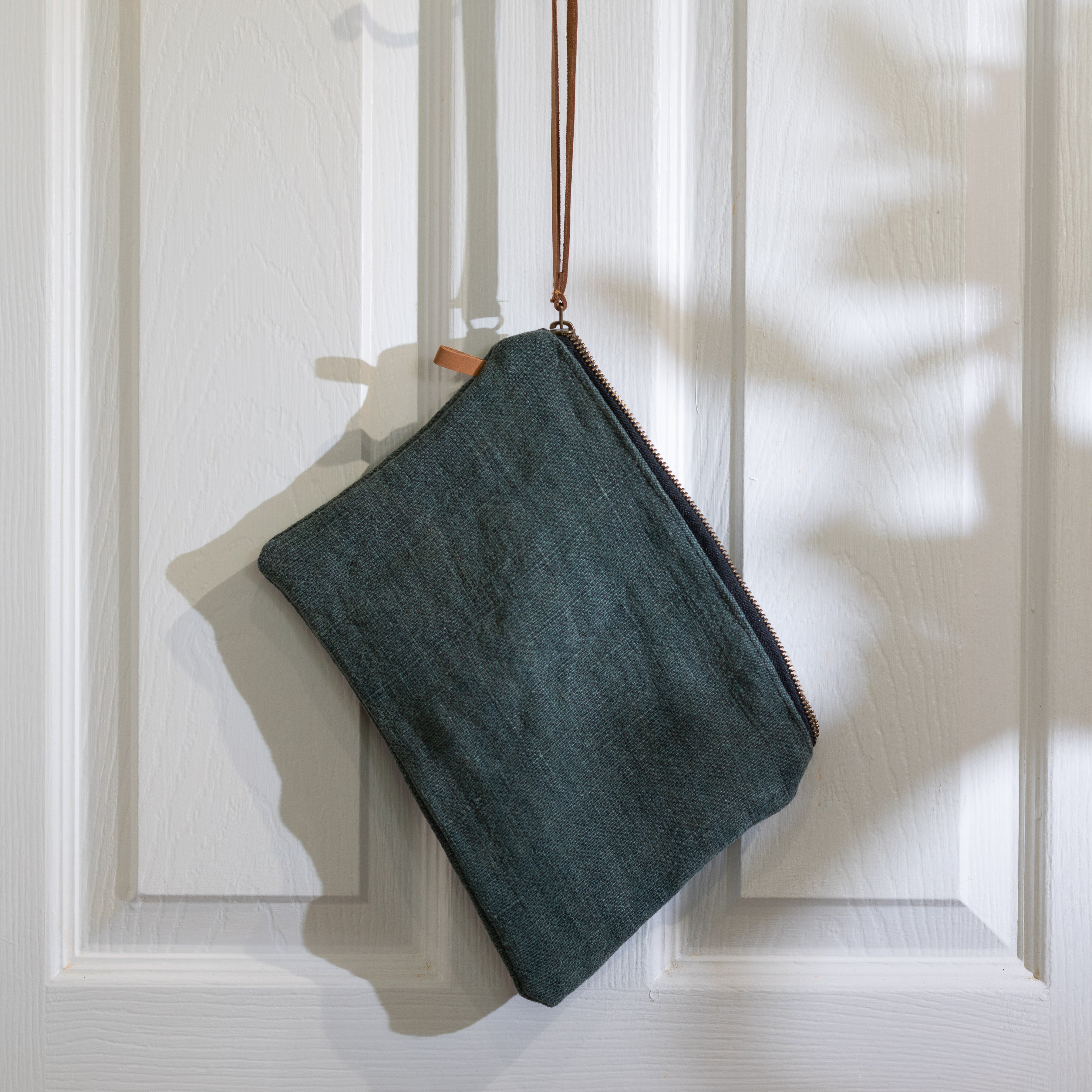 Grey jute bag with leather strap hanging on white door.
