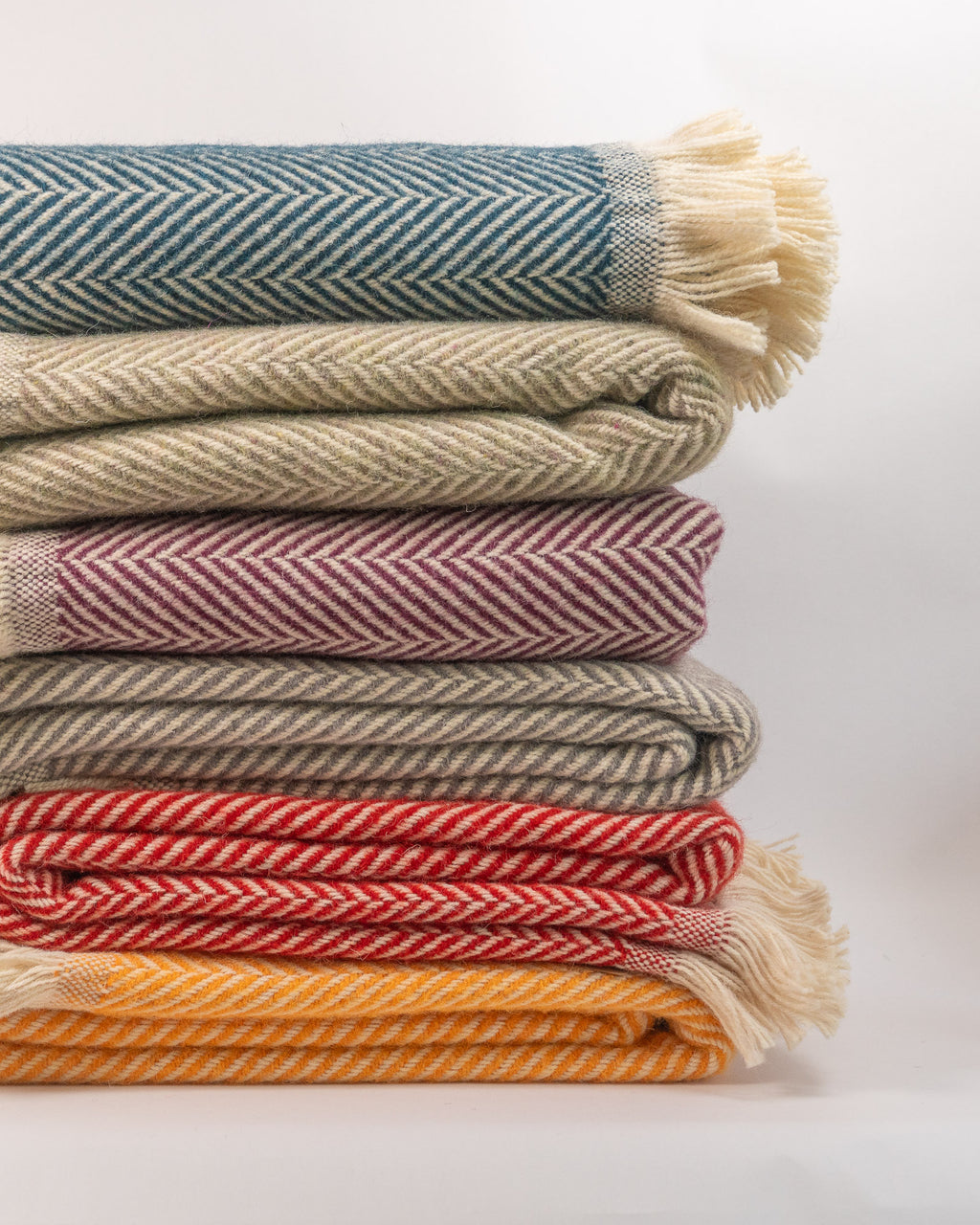 Stack of colorful woven blankets on a light background - blnakets are all 100% recycled wool.