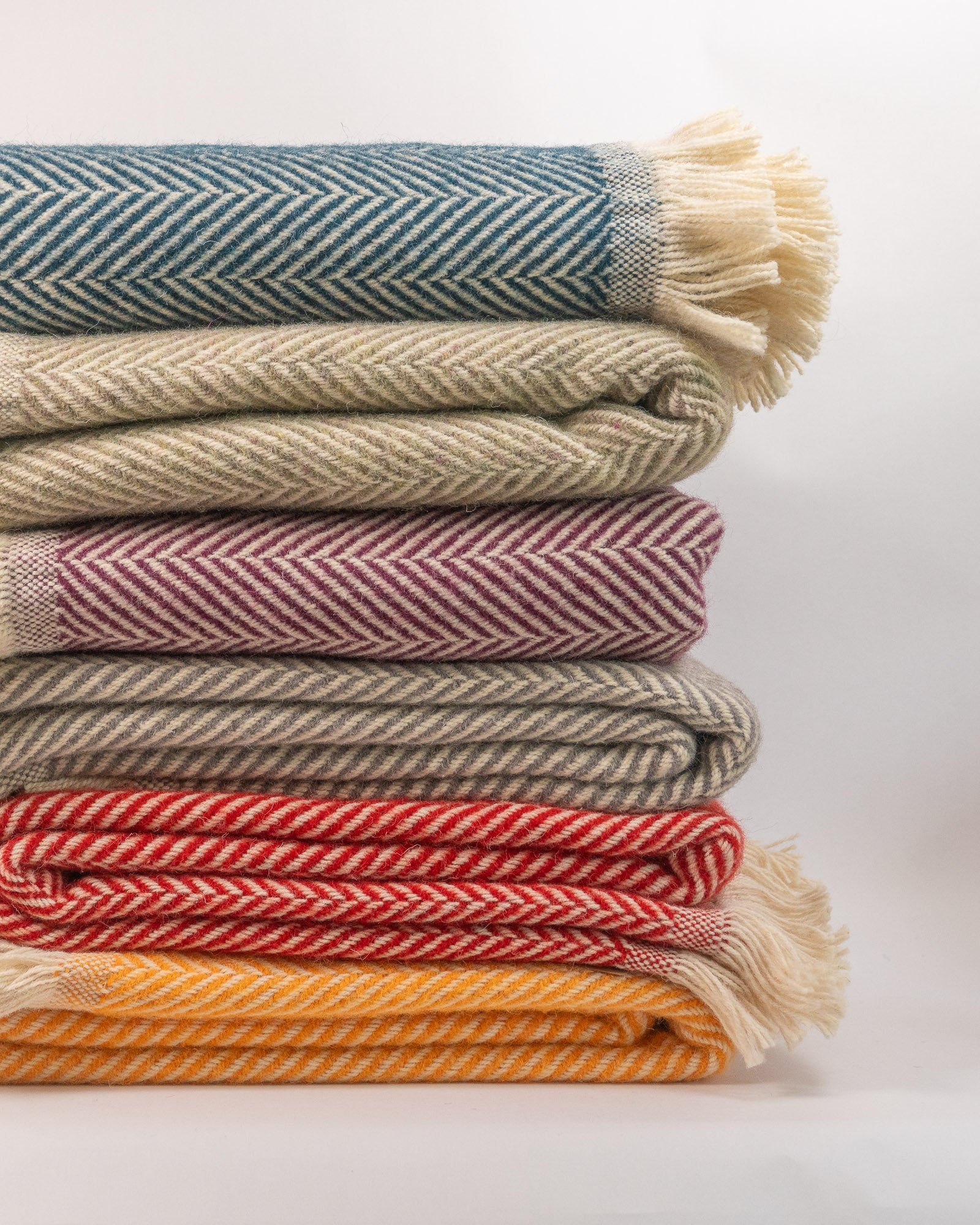 Stack of colorful woven blankets on a light background - blnakets are all 100% recycled wool.
