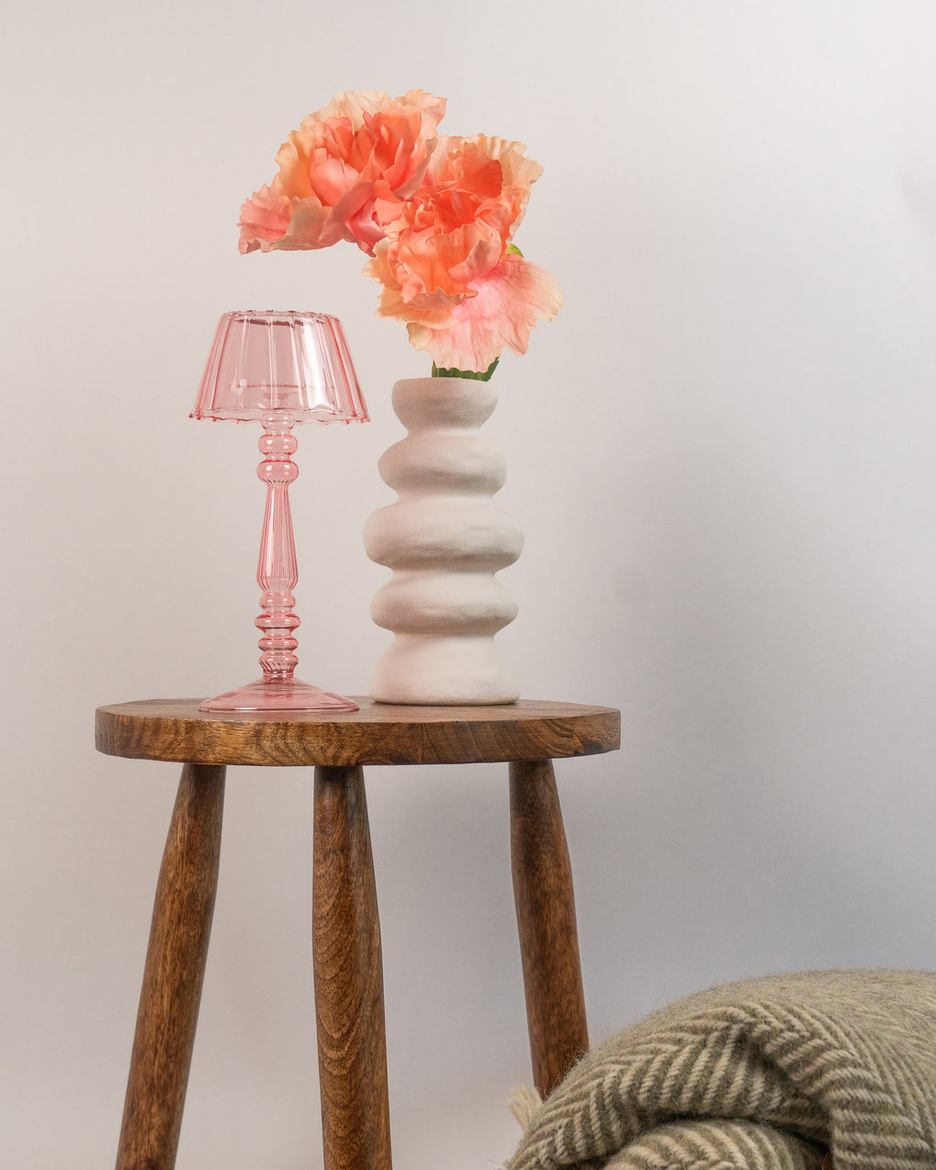 Small wooden table with a pink lamp and white vase holding orange flowers on a plain background