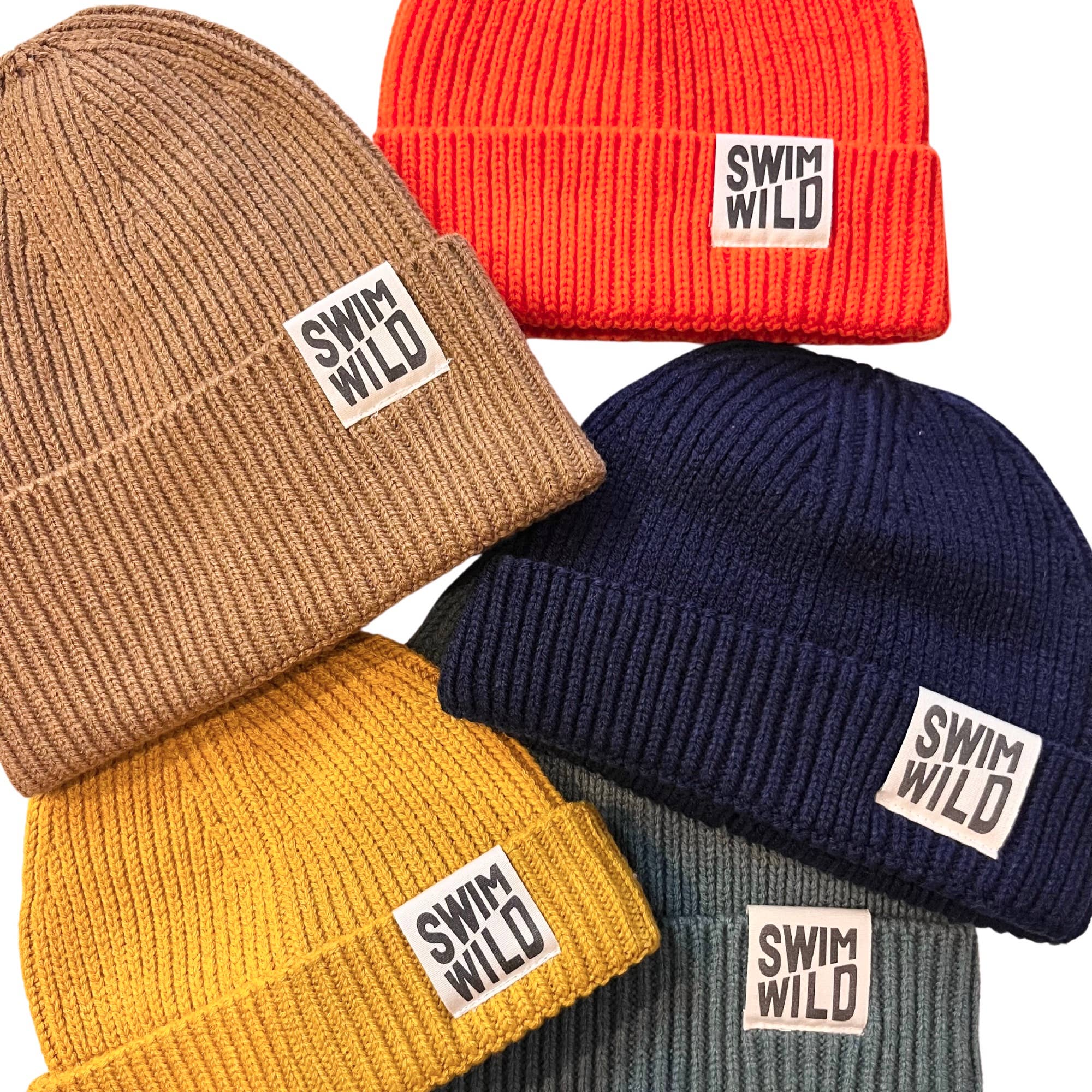 Five knitted fishermans style beanie hats in different colours; bright orange, light brown, navy, mustard yellow and ocean grey. Each hat has a motif reading 'SWIM WILD'. 