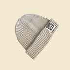 Oat coloured cosy fisherman style beanie hat on cream background. Text on hat reads "SWIM WILD". Great sustainable gift for Wild Swimmers