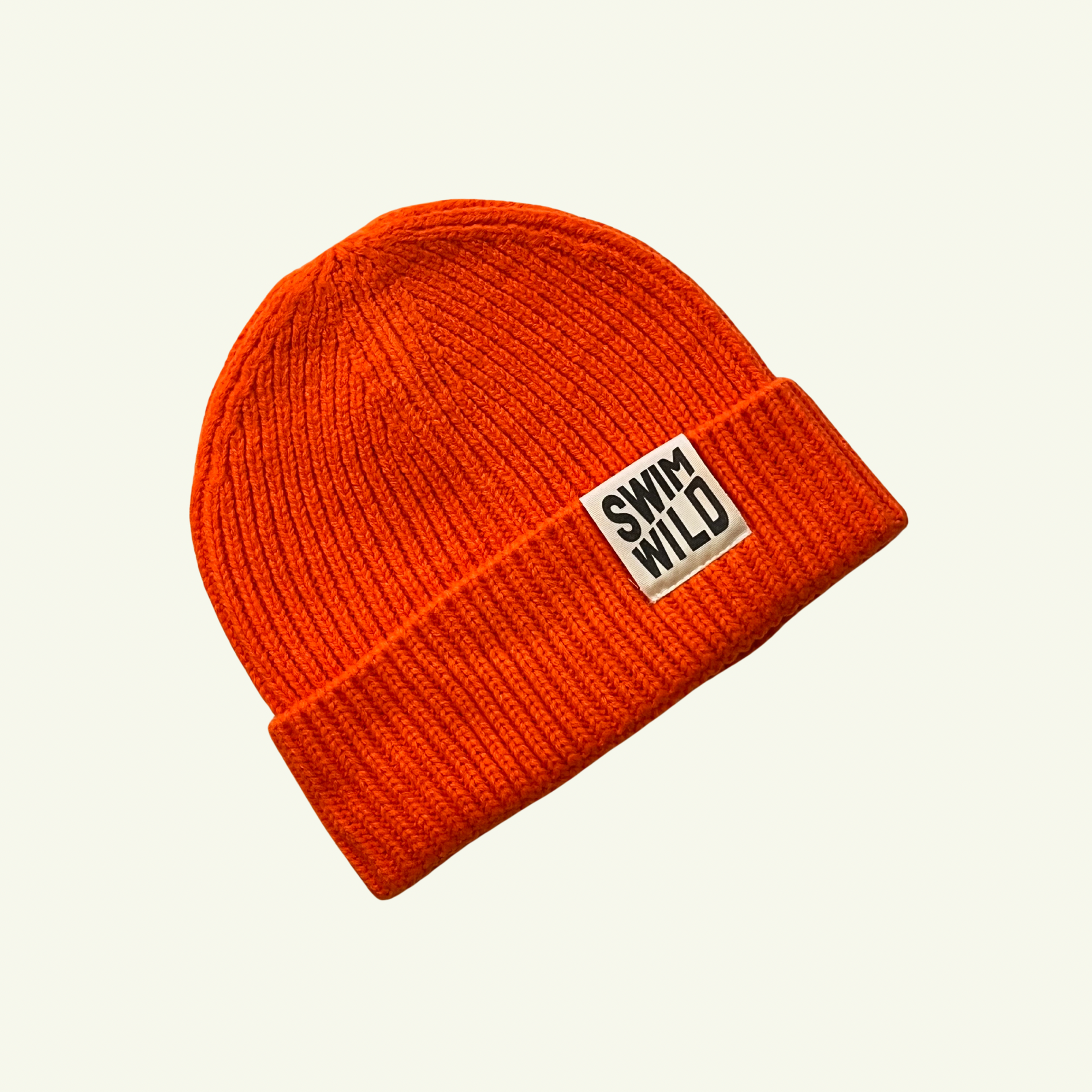 Orange cosy fisherman style beanie hat on cream background. Text on hat reads "SWIM WILD". 
Great sustainable gift for Wild Swimmers