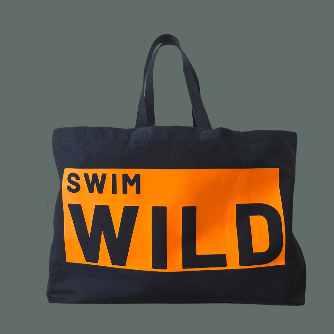 Jumbo navy thick cotton bag on grey background. Large orange text box on bag with text " SWIM WILD" in navy.