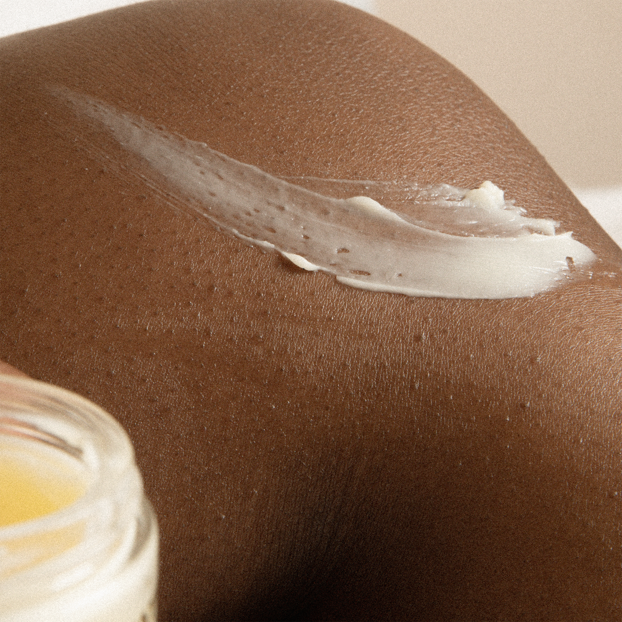 Part of a body with  MIRROR WATER RUB balm on skin showing consistency of balm. Partial product jar in shot.
