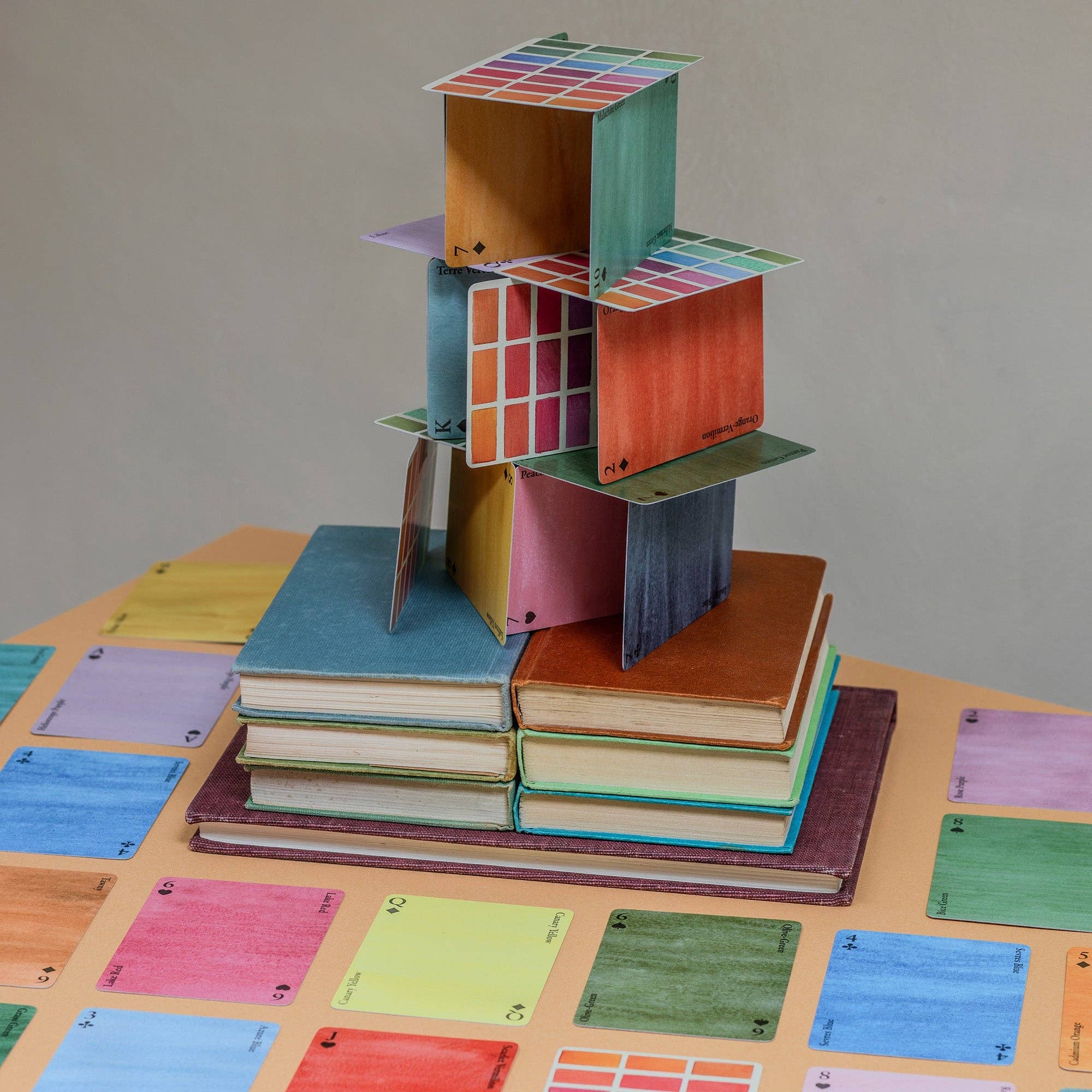 Multicoloured playing cards, balance stacked on books. Cards are styled as colour swatches with visable brush strokes.