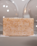 Unwrapped Exfoliating soap. Tet on soap reads "PURE VEGETABLE SOAP, MADE IN ENGLAND" Bubbles on soap and large bubbles in background.