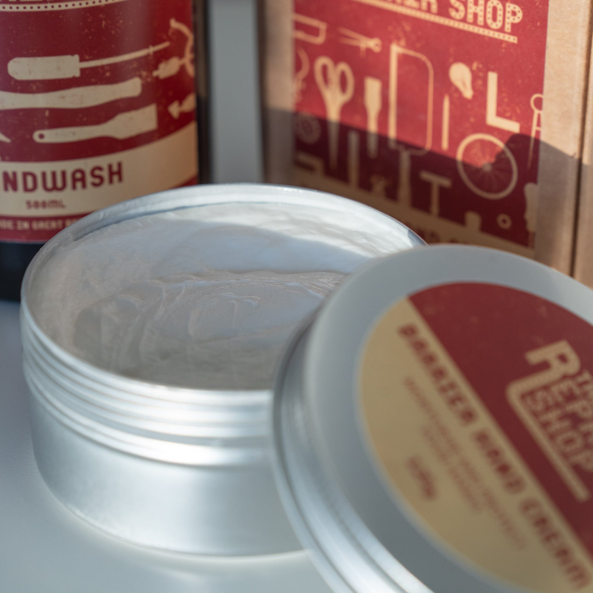 Close up showing The Repair Shop Barrier Cream which is a rich moisturising white cream. Packaging shown in background.