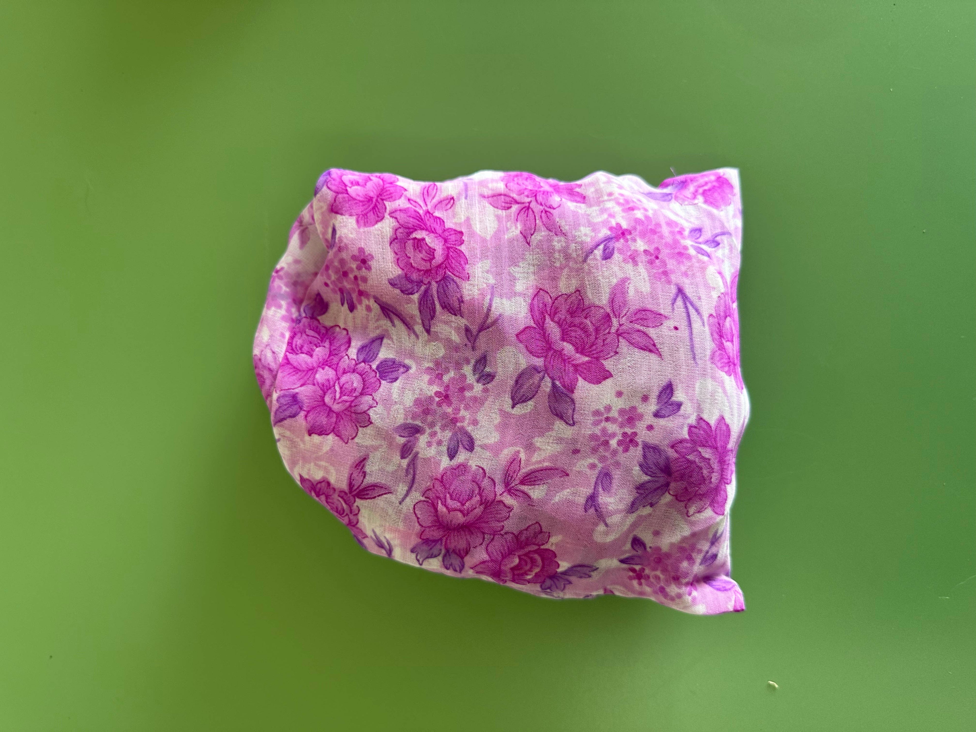 Fairtrade shopping bag rolled into pouch - fabric in purple floral pattern on green background.