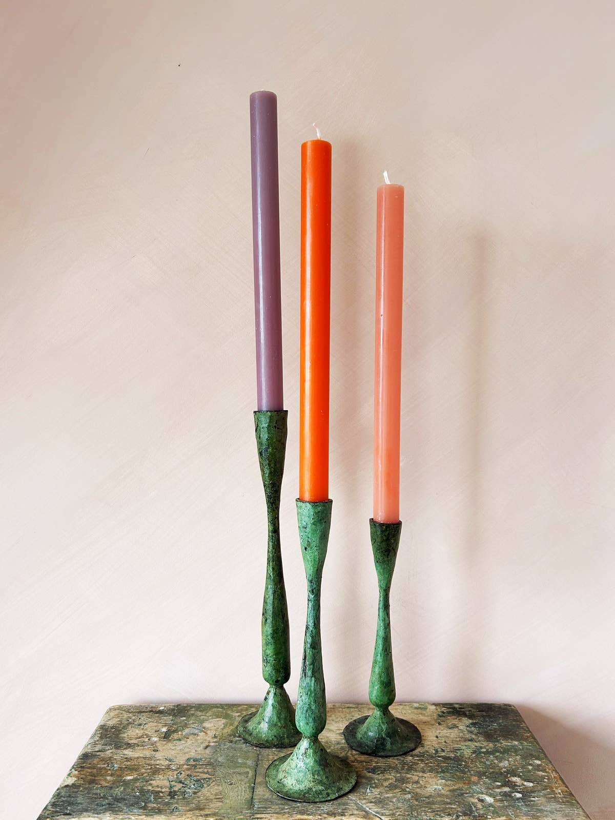 Group of small , medium and large candlesticks with colourful candles, on small rustic table. Hand forged candlesticks , ethically made.