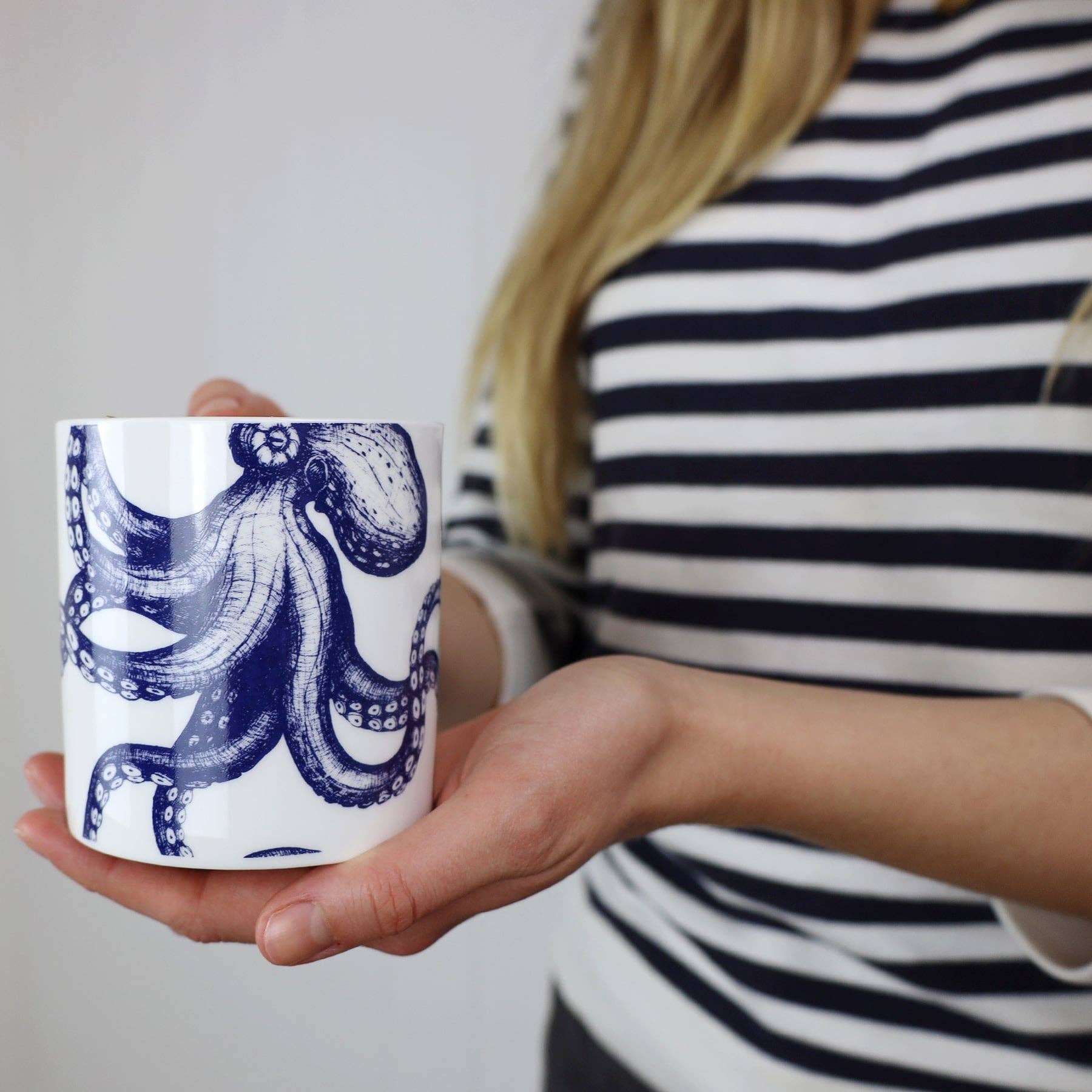 Model in navy and white stripe top is holding octopus mug - close up of illustration on mug.