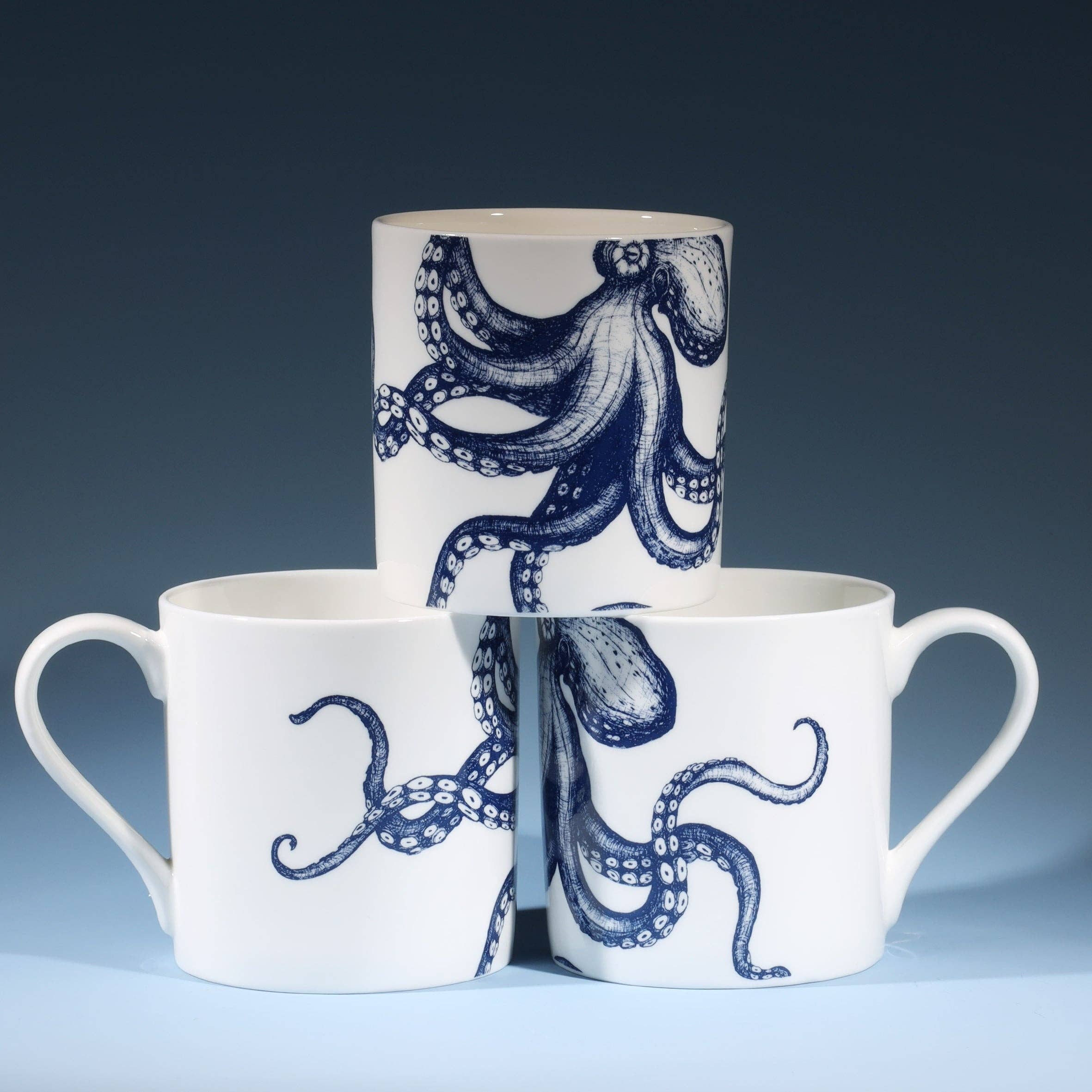 Stack of three octopus mugs showing different angles of octopus illustration. Studio shot on inky blue background.