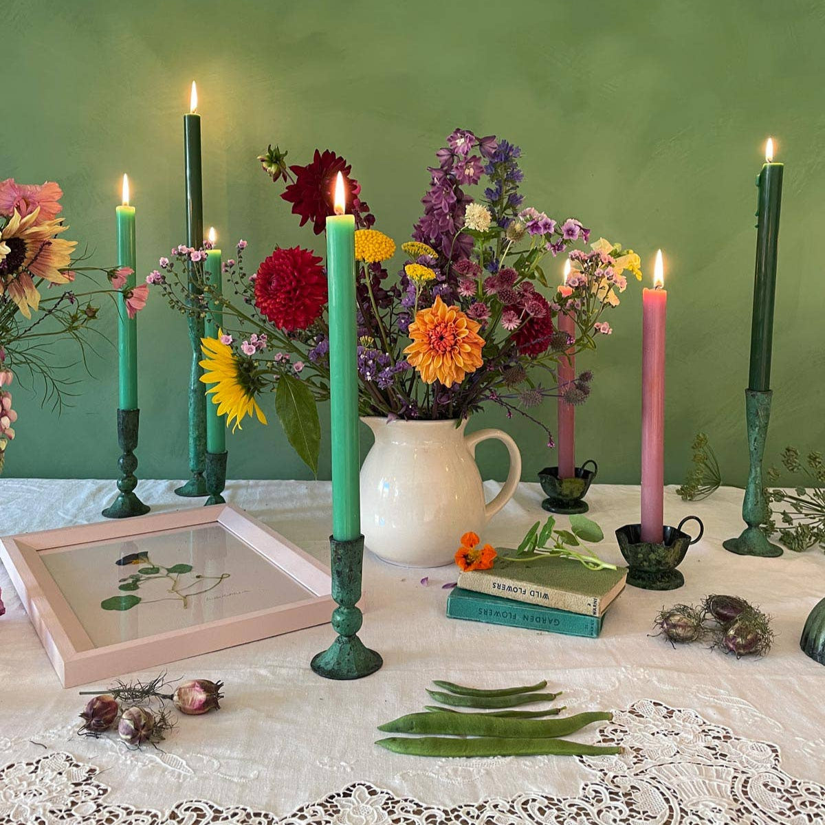 Colourful table top with collection of candlesticks and colourful flowers and candles.Summer feeling with flowerheads and garden peas on table top.