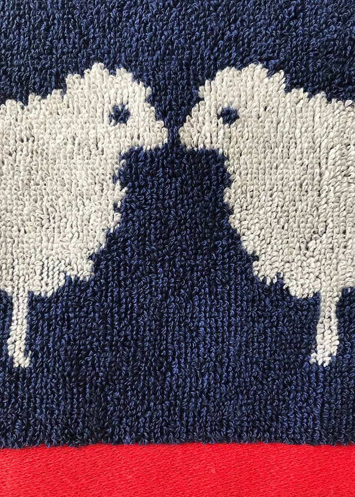 Close-up of a jacquard weave 100% organic cotton Kissing Sheep towel with white and navy pattern on a red background. Made by Anorak.
