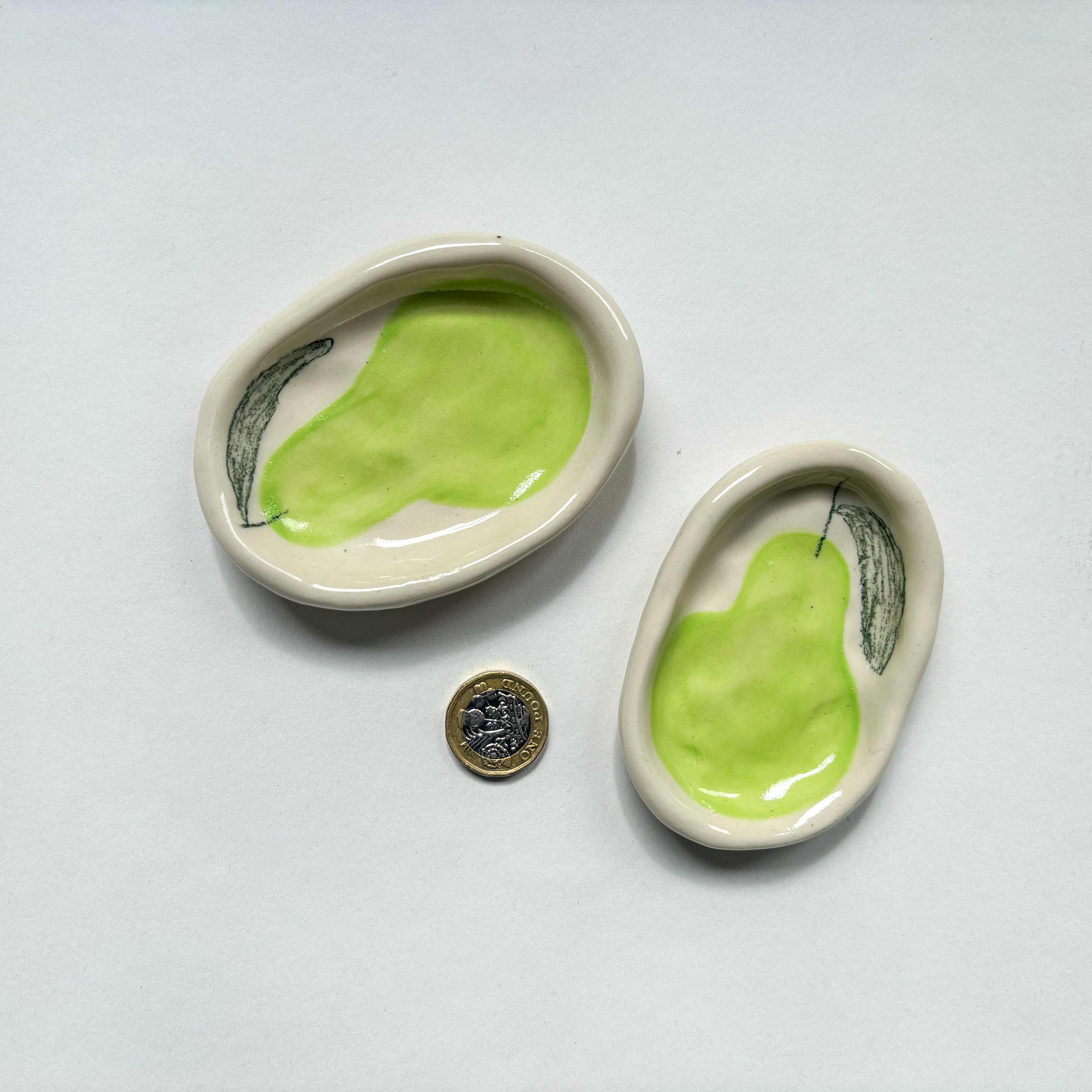 Two  handmade ceramic dishes with green pear design  are shown beside a pound coin for scale.